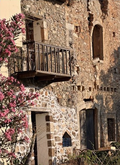 A weathered Cretan stone house framed by pink flowers